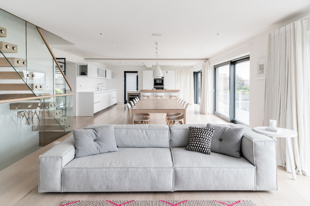 Inspiration for a large contemporary open plan living room in Cornwall with white walls, light hardwood flooring, a two-sided fireplace, a plastered fireplace surround and white floors.