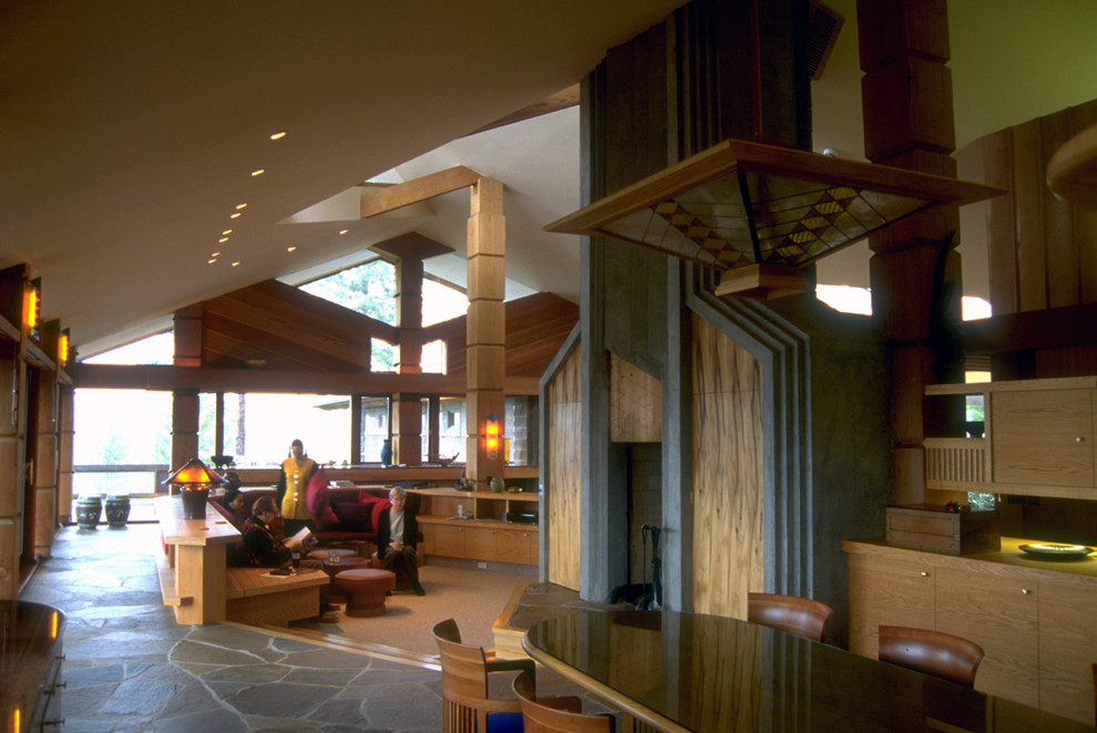 Пример оригинального дизайна: огромная открытая гостиная комната в современном стиле с с книжными шкафами и полками, разноцветными стенами, полом из сланца, двусторонним камином и фасадом камина из камня без телевизора