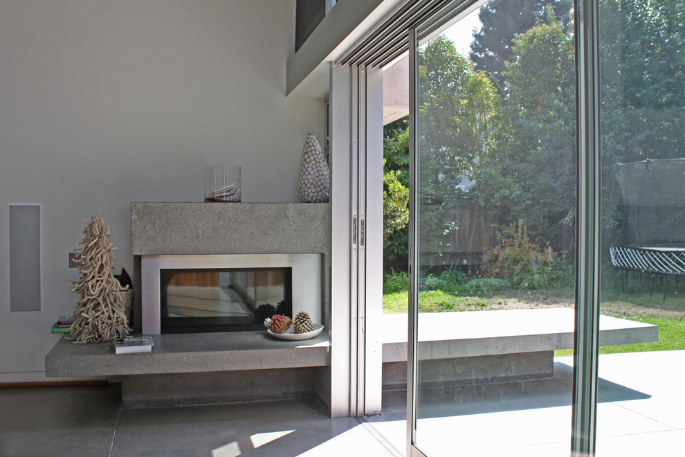 На фото: большая двухуровневая гостиная комната в стиле ретро с серыми стенами, бетонным полом и фасадом камина из бетона с