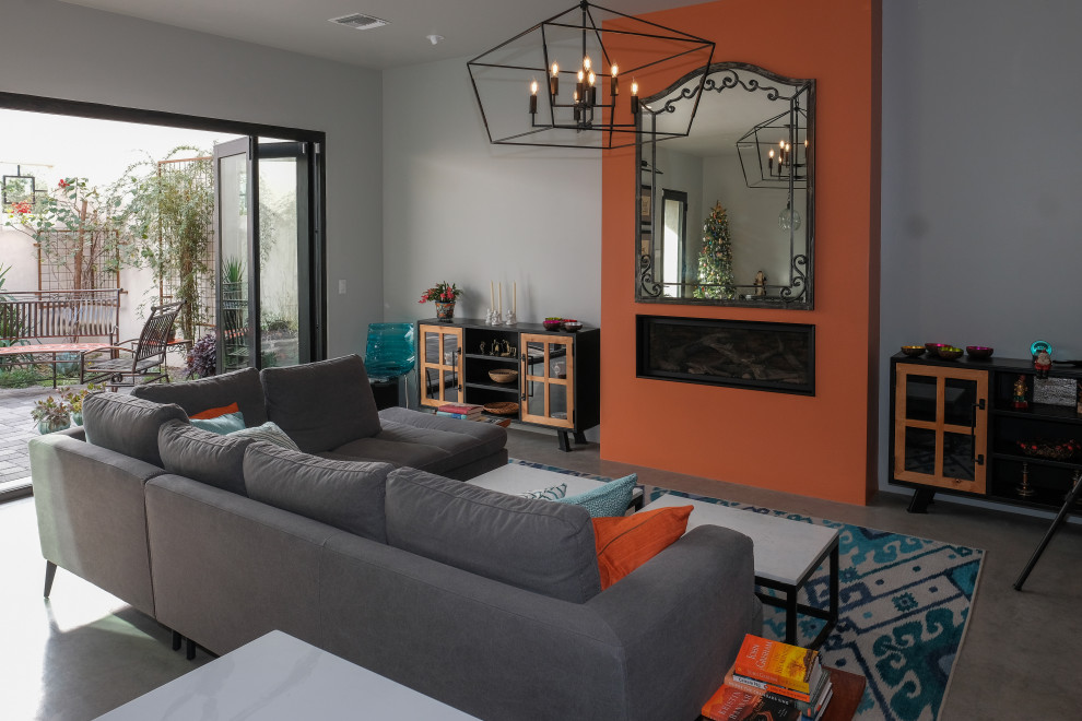 Réalisation d'un salon design ouvert avec un mur orange, sol en béton ciré, une cheminée standard, un manteau de cheminée en plâtre et un sol gris.