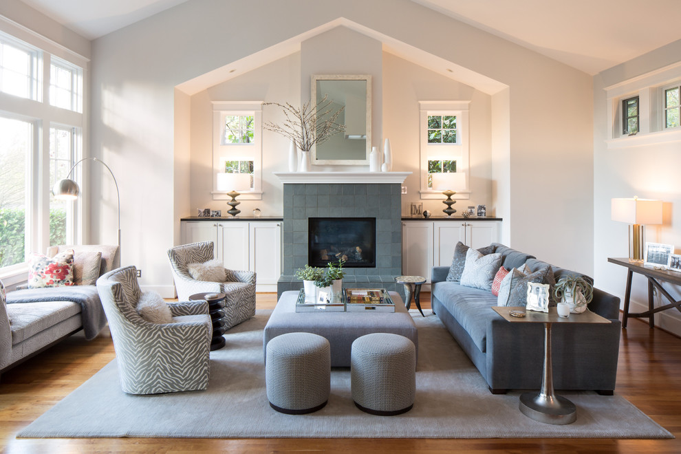 Cette photo montre un grand salon tendance ouvert avec un mur gris, un sol en bois brun, une cheminée standard, un manteau de cheminée en carrelage et aucun téléviseur.