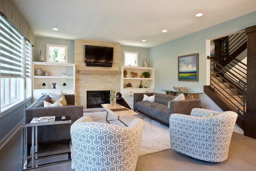 Пример оригинального дизайна: открытая гостиная комната в стиле кантри с синими стенами, паркетным полом среднего тона, стандартным камином, фасадом камина из камня, телевизором на стене и коричневым полом