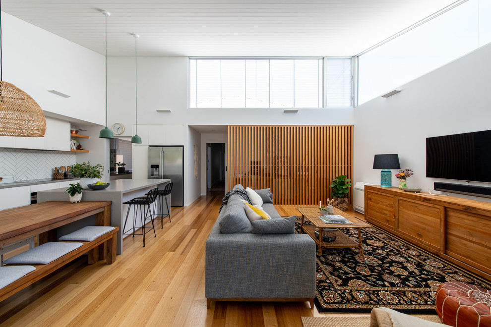 This is an example of a contemporary open plan living room in Newcastle - Maitland with white walls, medium hardwood flooring, a wall mounted tv, brown floors and feature lighting.