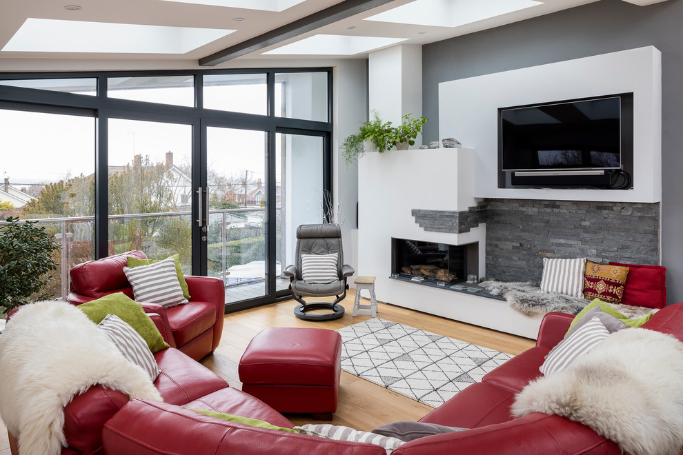 Design ideas for a modern formal open plan living room in Essex with grey walls, light hardwood flooring, a corner fireplace, a plastered fireplace surround, a wall mounted tv and brown floors.