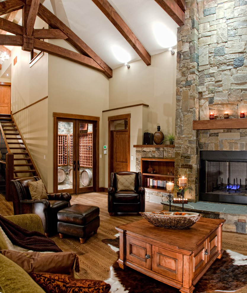 Aménagement d'un salon montagne ouvert avec une salle de réception, un mur beige, un sol en bois brun, une cheminée standard, un manteau de cheminée en pierre, aucun téléviseur et un escalier.