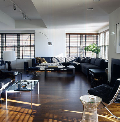 Exemple d'un grand salon mansardé ou avec mezzanine moderne avec un mur blanc, un sol en bois brun, une cheminée standard, un manteau de cheminée en pierre, un téléviseur indépendant, un sol marron et canapé noir.