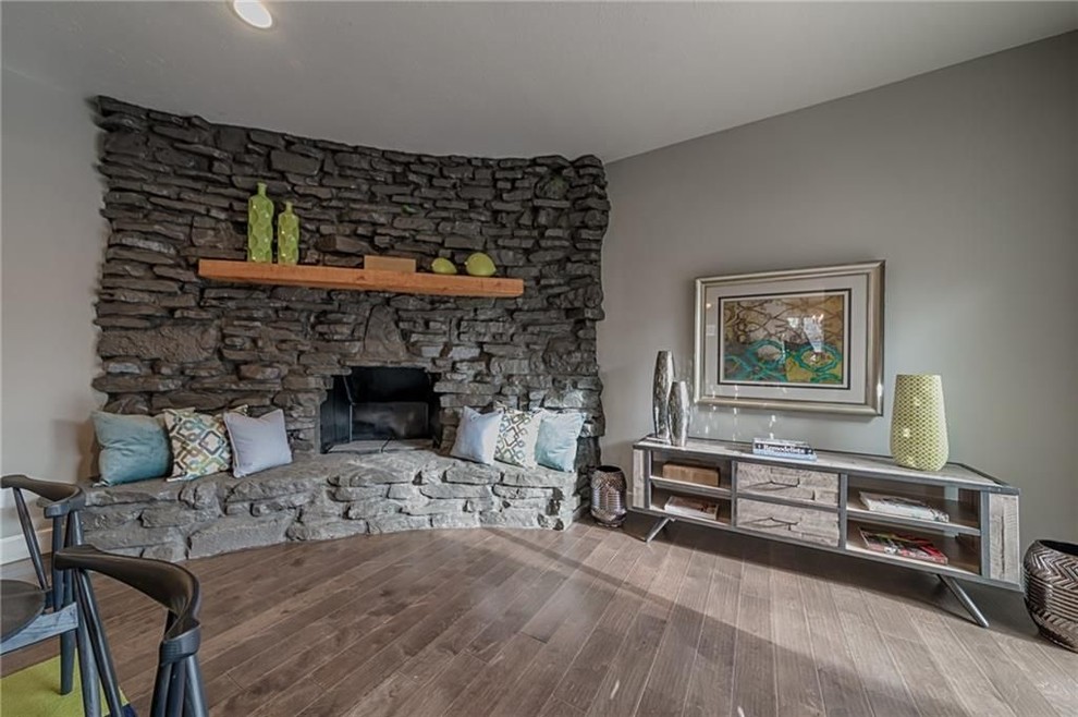 Ejemplo de salón abierto retro de tamaño medio con paredes grises, suelo de madera en tonos medios, chimenea de esquina y marco de chimenea de piedra
