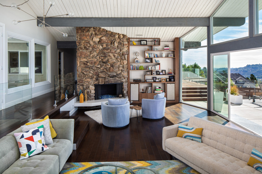 Inspiration for a large 1960s open concept dark wood floor, brown floor and vaulted ceiling living room remodel in Los Angeles with white walls, a corner fireplace, a stone fireplace and no tv