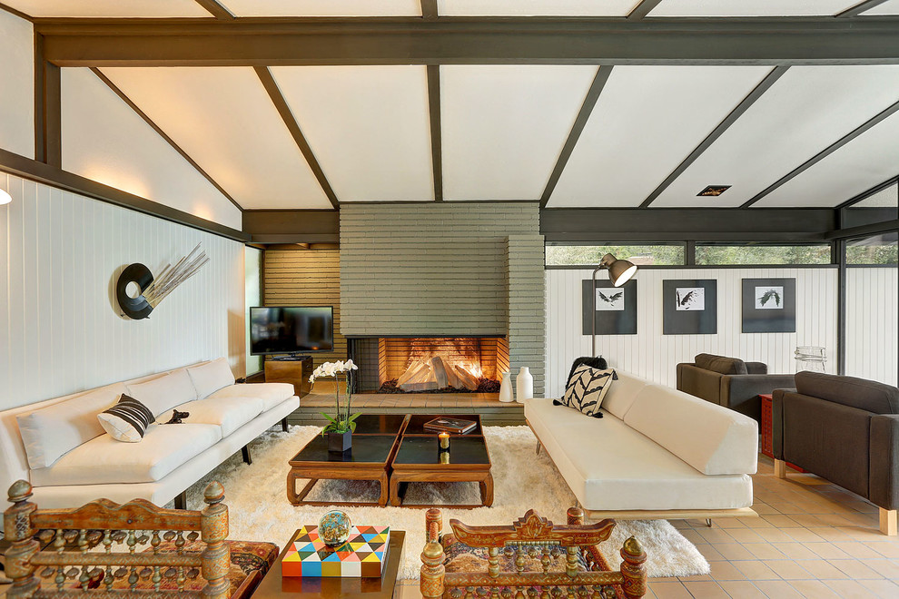 На фото: большая открытая гостиная комната в стиле ретро с белыми стенами, стандартным камином, фасадом камина из кирпича и отдельно стоящим телевизором