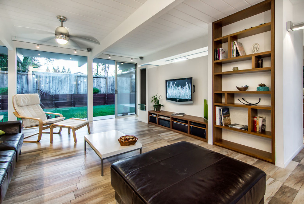 Пример оригинального дизайна: открытая гостиная комната среднего размера в стиле модернизм с белыми стенами, телевизором на стене, с книжными шкафами и полками, полом из керамогранита и бежевым полом