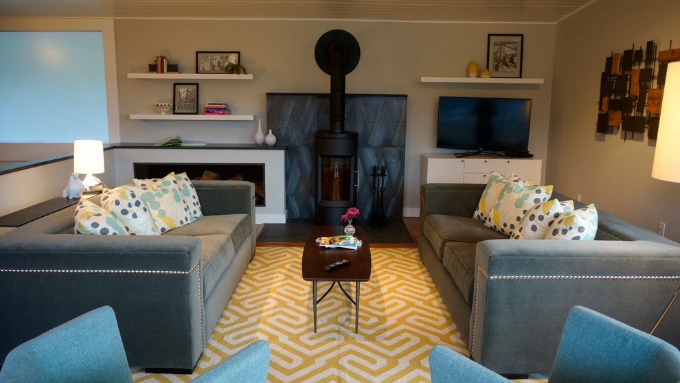 Imagen de salón abierto retro de tamaño medio con paredes grises, suelo de bambú, estufa de leña, marco de chimenea de metal y televisor independiente
