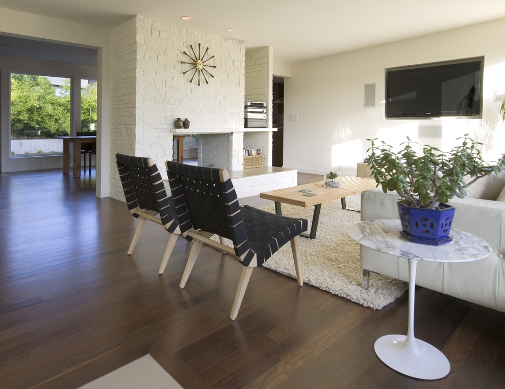 Стильный дизайн: гостиная комната в стиле модернизм с коричневым полом, белыми стенами, фасадом камина из кирпича, телевизором на стене и ковром на полу - последний тренд