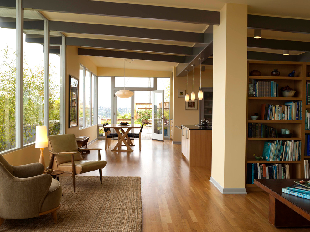 Esempio di un grande soggiorno minimalista aperto con libreria, pareti gialle, pavimento in legno massello medio e nessun camino