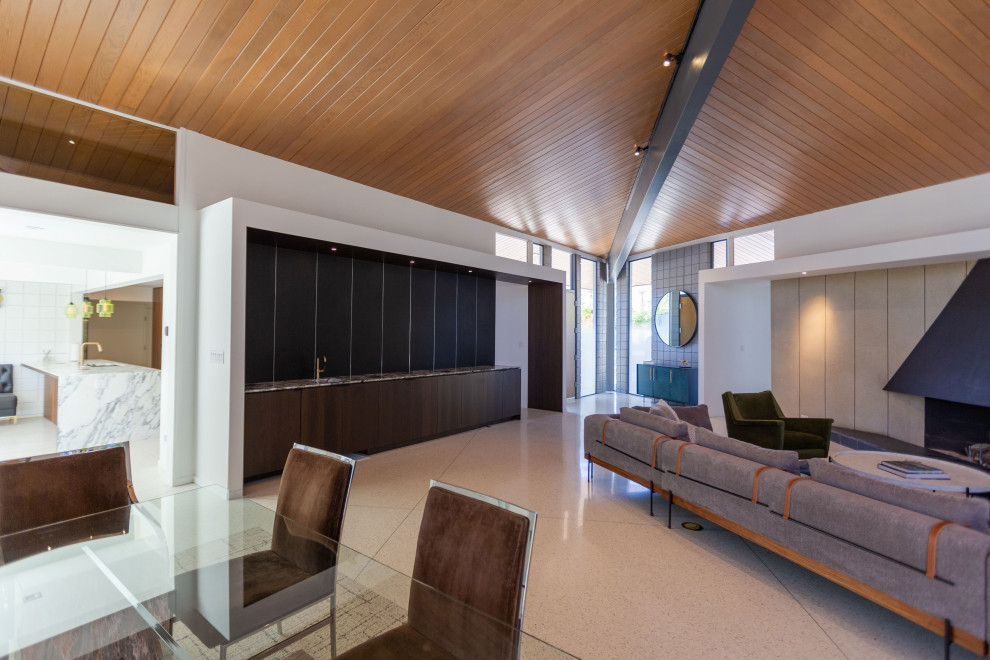 Inspiration for a large midcentury open plan living room in Other with a home bar, white walls, a standard fireplace, a metal fireplace surround, a wall mounted tv, white floors and a vaulted ceiling.
