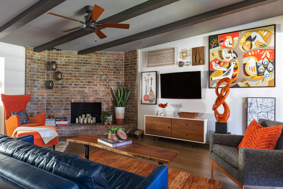Photo of a midcentury open plan living room in Houston with white walls, medium hardwood flooring, a standard fireplace, a brick fireplace surround, a wall mounted tv, brown floors, exposed beams and brick walls.