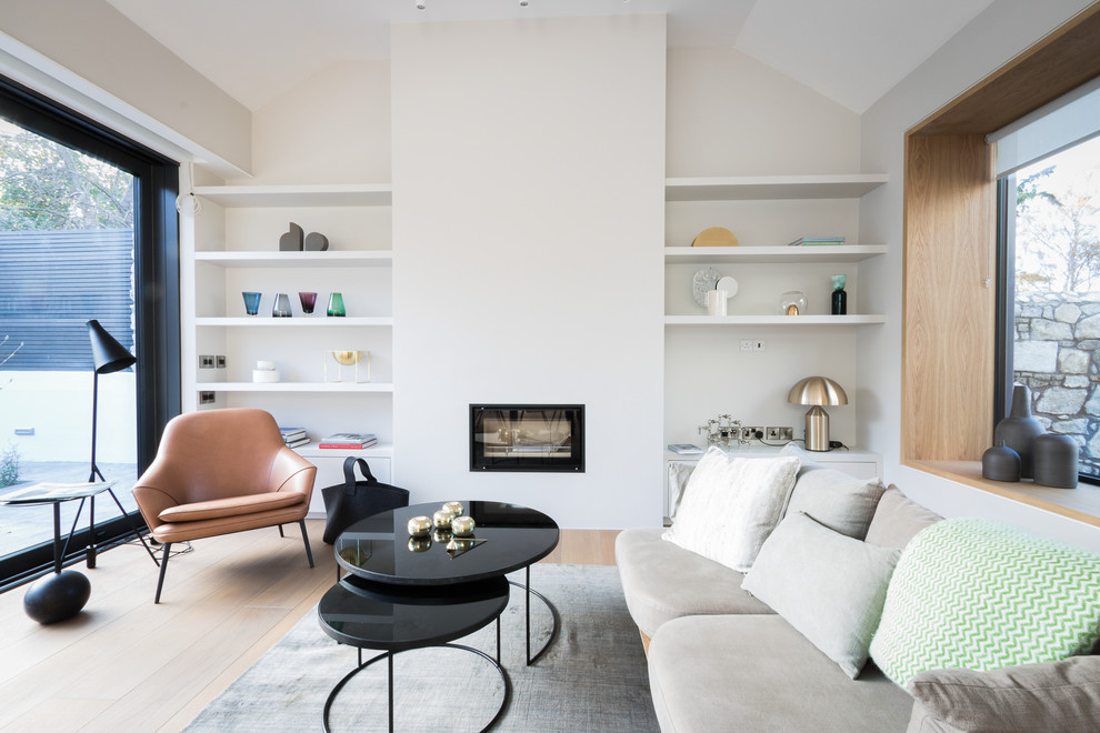 Imagen de biblioteca en casa contemporánea de tamaño medio con paredes blancas, suelo de madera clara y chimenea lineal