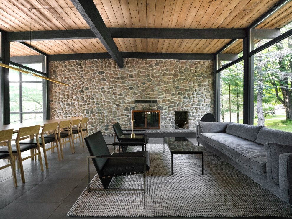 Cette photo montre un salon rétro ouvert avec un mur gris, une cheminée standard, un manteau de cheminée en pierre, un sol gris, poutres apparentes et un plafond en bois.