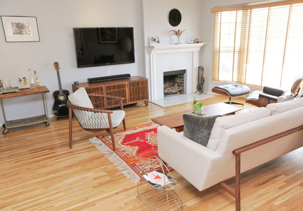 Источник вдохновения для домашнего уюта: открытая гостиная комната среднего размера в стиле ретро с серыми стенами, паркетным полом среднего тона, стандартным камином, фасадом камина из дерева, телевизором на стене и коричневым полом