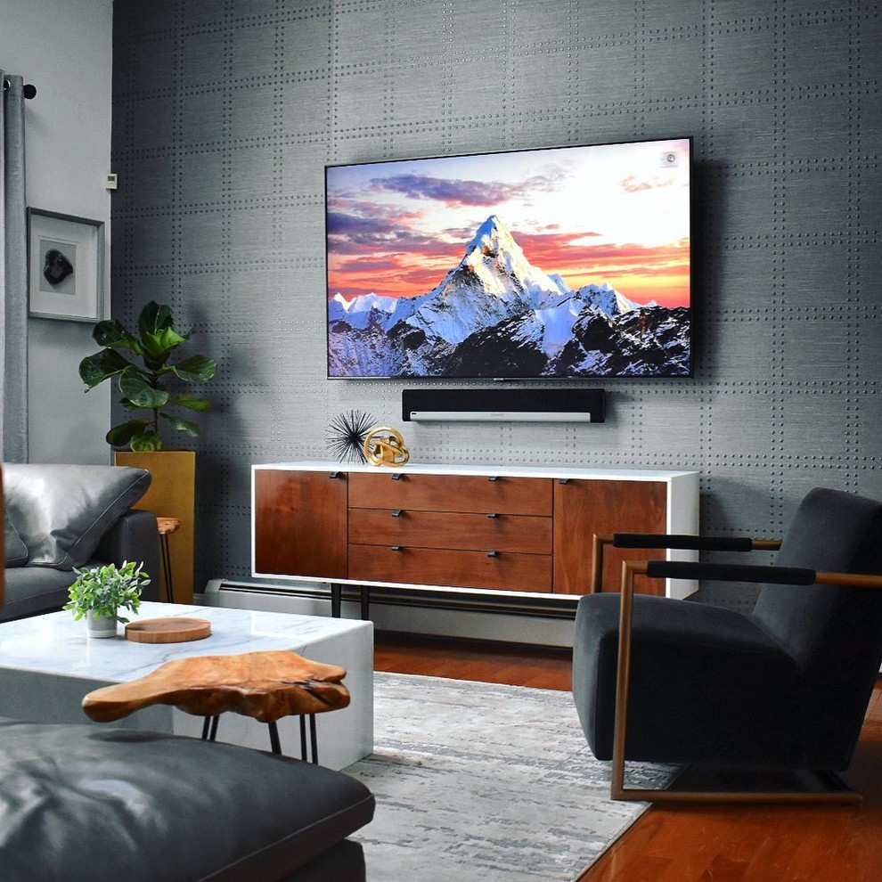 Cette image montre un salon vintage ouvert avec un mur gris, un sol en bois brun, un téléviseur fixé au mur, un sol marron, un plafond voûté et du papier peint.