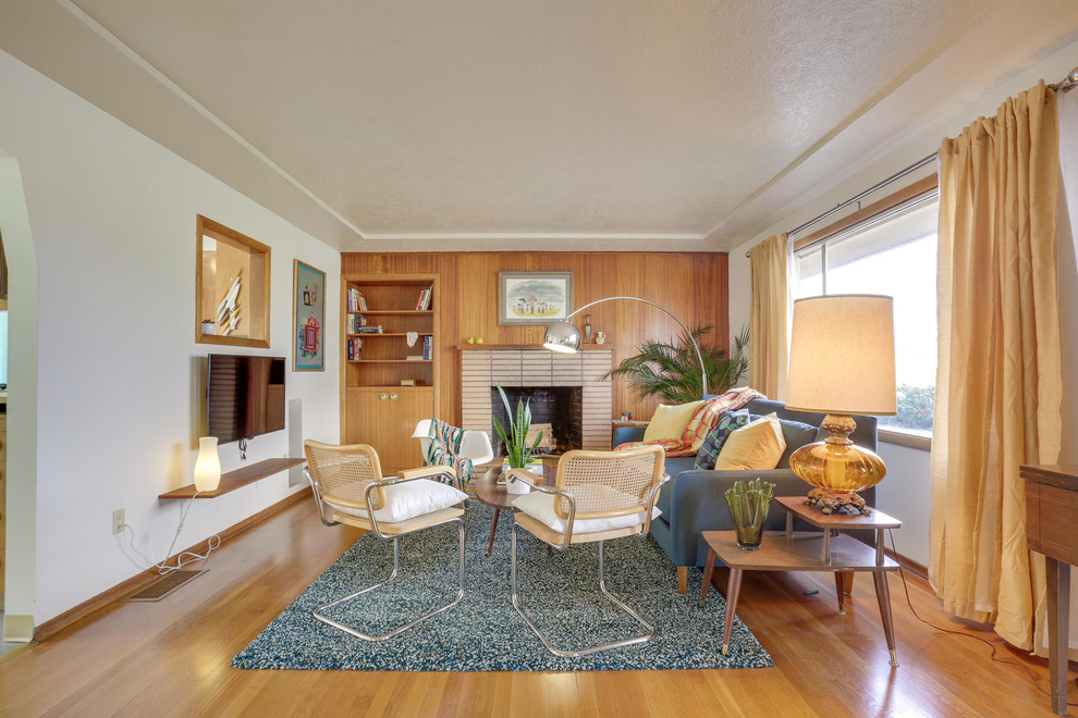Mittelgroßes, Abgetrenntes Retro Wohnzimmer mit weißer Wandfarbe, braunem Holzboden, Kamin, Kaminumrandung aus Backstein, TV-Wand und braunem Boden in Portland