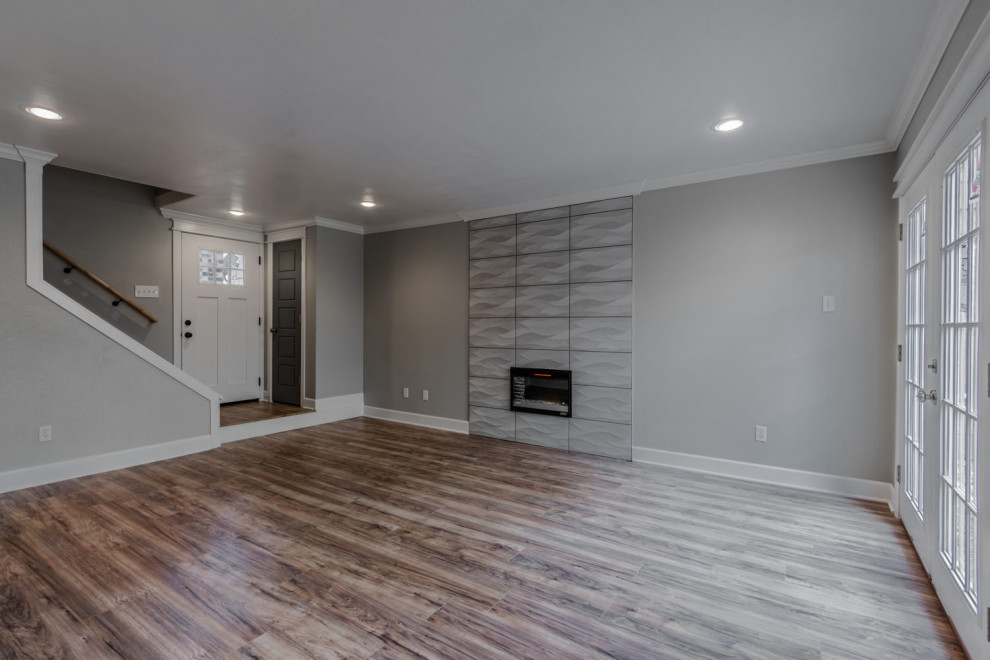 Свежая идея для дизайна: открытая гостиная комната среднего размера в стиле ретро с серыми стенами, полом из ламината, стандартным камином, фасадом камина из плитки, коричневым полом и многоуровневым потолком - отличное фото интерьера