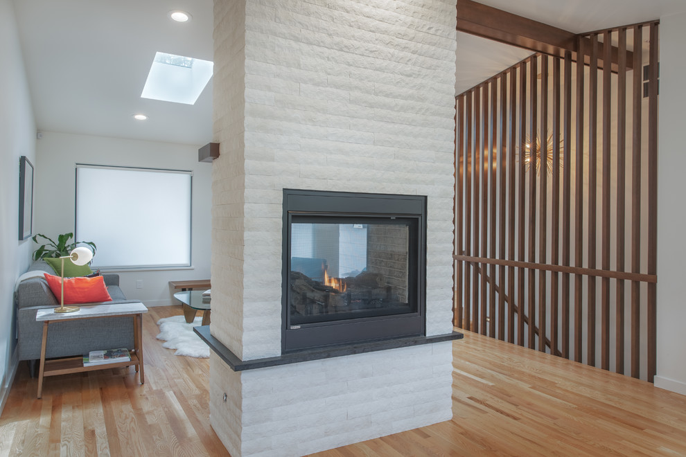 Example of a mid-century modern light wood floor, multicolored floor and vaulted ceiling living room design in Seattle with white walls, a two-sided fireplace and a brick fireplace