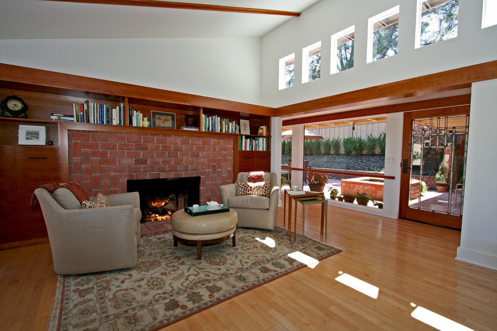 Immagine di un soggiorno moderno con pareti bianche, parquet chiaro, camino classico e cornice del camino in mattoni