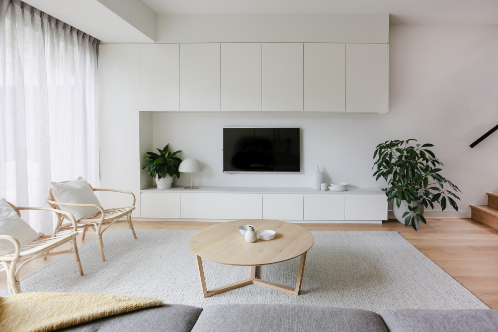 Imagen de salón abierto actual con paredes blancas, suelo de madera en tonos medios, televisor colgado en la pared y suelo marrón