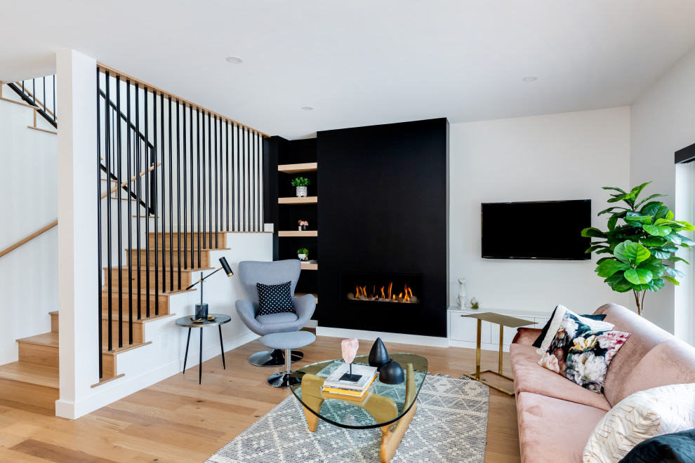Esempio di un soggiorno minimal di medie dimensioni e aperto con pareti bianche, parquet chiaro, camino classico, TV a parete e pavimento marrone