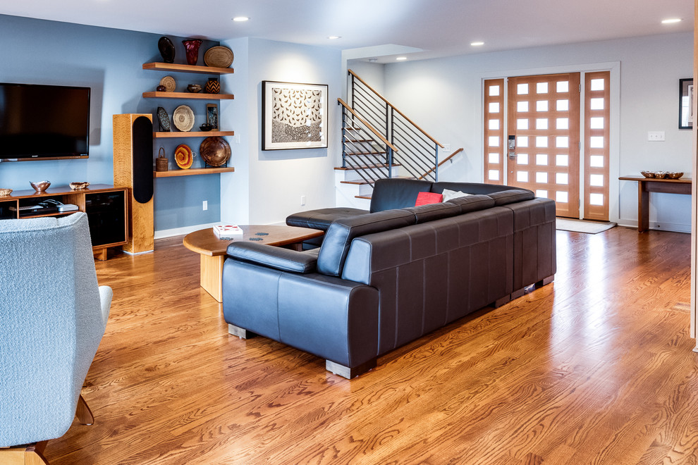 Immagine di un soggiorno design di medie dimensioni e aperto con pavimento in legno massello medio, nessun camino, TV a parete, pavimento marrone e pareti blu