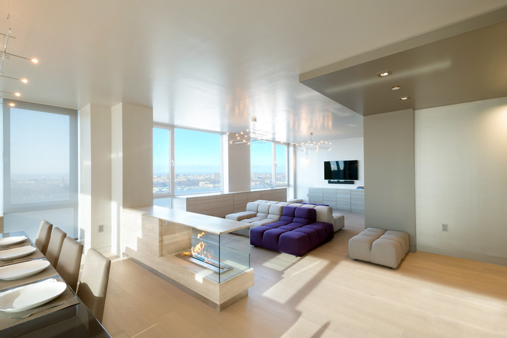 Идея дизайна: большая открытая гостиная комната в современном стиле с серыми стенами, двусторонним камином, фасадом камина из камня, телевизором на стене и светлым паркетным полом