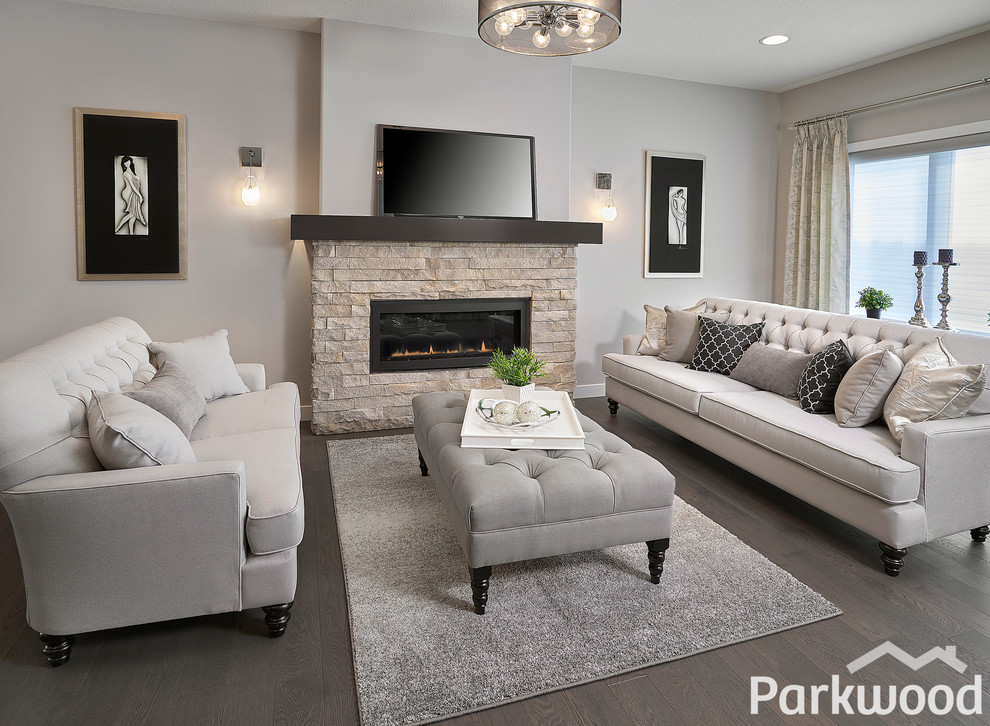 Repräsentatives, Offenes Shabby-Look Wohnzimmer mit grauer Wandfarbe, braunem Holzboden, Kamin, Kaminumrandung aus Stein und TV-Wand in Edmonton