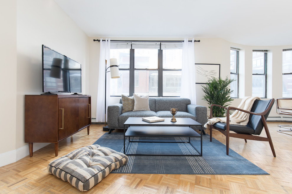 Example of a trendy open concept light wood floor and brown floor living room design in Boston with beige walls and a tv stand