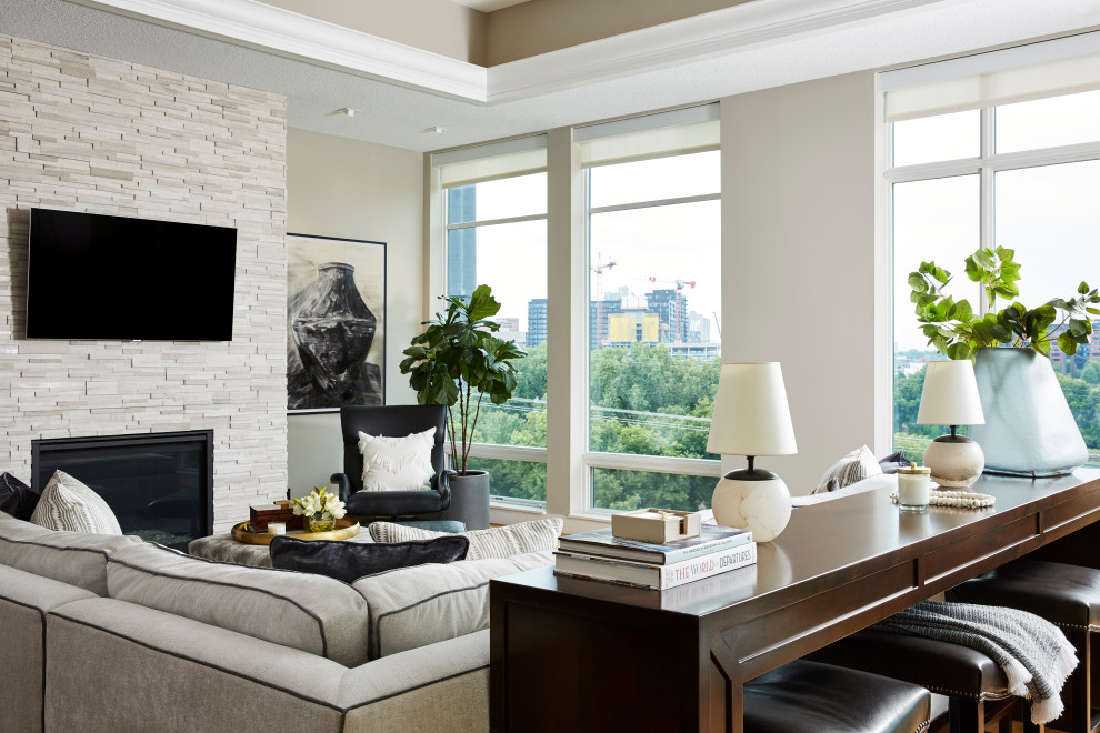 Cette image montre un grand salon minimaliste ouvert avec un mur beige, un sol en bois brun, une cheminée standard, un manteau de cheminée en pierre de parement et un téléviseur fixé au mur.