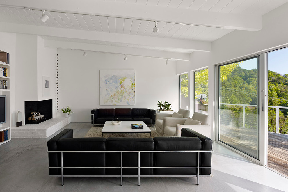 Foto di un soggiorno minimalista aperto con camino ad angolo, libreria, pareti bianche, pavimento in cemento, cornice del camino in intonaco e parete attrezzata