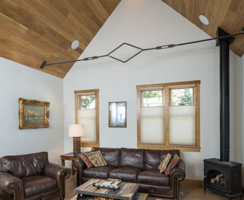Diseño de salón abierto rural de tamaño medio con paredes blancas, suelo de madera clara, estufa de leña y marco de chimenea de metal