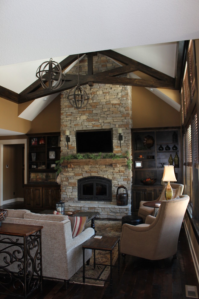 Example of a large mountain style dark wood floor living room design in Kansas City with beige walls, a wood stove, a stone fireplace and a media wall