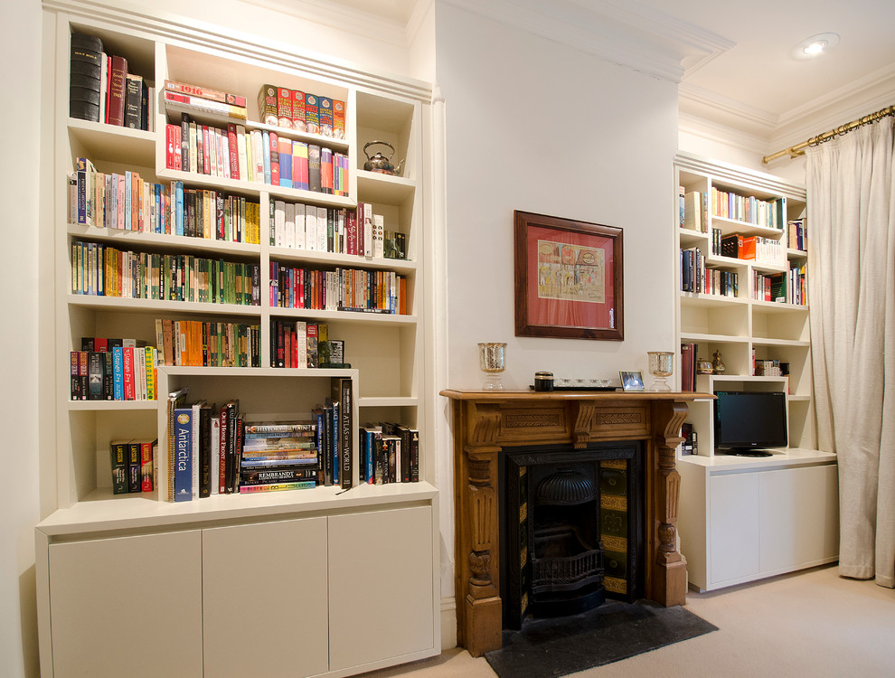 Bild på ett litet funkis separat vardagsrum, med vita väggar, heltäckningsmatta, en standard öppen spis, en spiselkrans i trä, en fristående TV, beiget golv och ett bibliotek