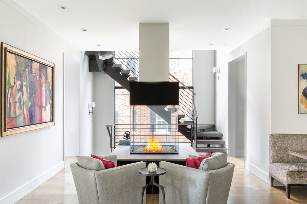 Idée de décoration pour un salon design ouvert avec un mur blanc, un sol en bois brun, une cheminée double-face et un escalier.