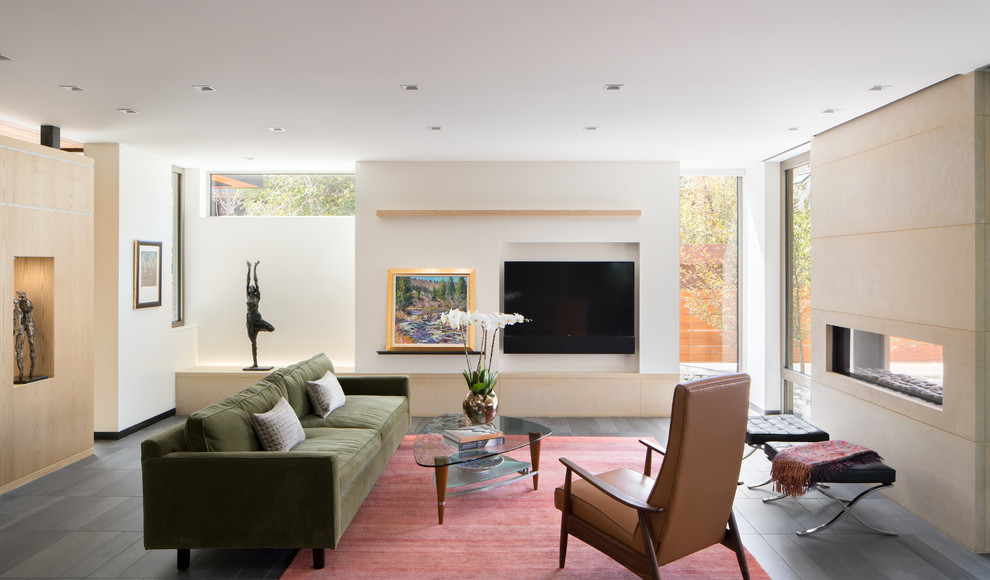 Пример оригинального дизайна: гостиная комната в современном стиле с белыми стенами, полом из керамической плитки, двусторонним камином, фасадом камина из камня и телевизором на стене