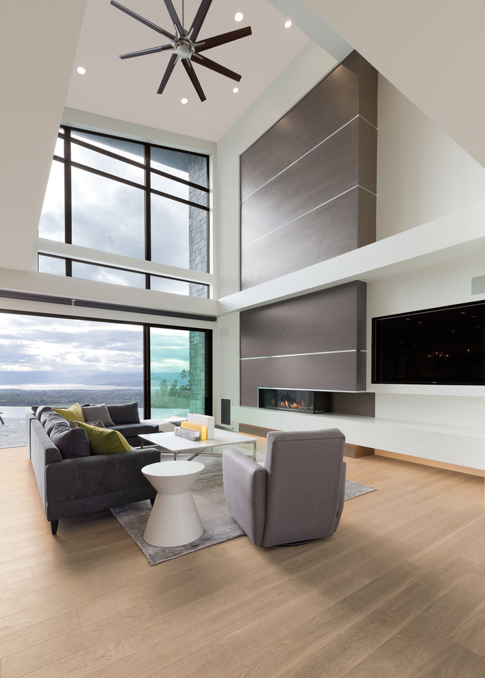 Esempio di un grande soggiorno moderno aperto con pareti bianche, parquet chiaro, camino ad angolo, cornice del camino in legno e TV a parete