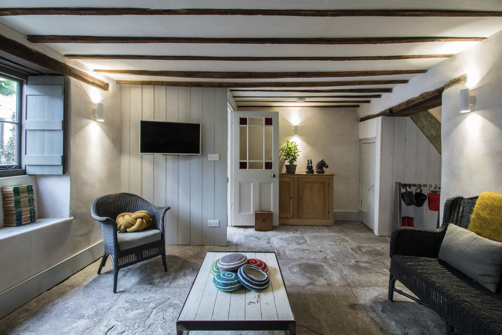 Imagen de salón abierto campestre pequeño con suelo de piedra caliza y televisor colgado en la pared