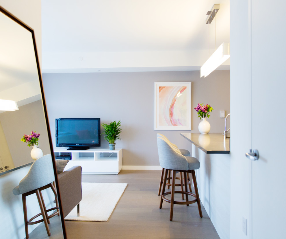 Cette image montre un petit salon design ouvert avec un mur gris et un sol en bois brun.