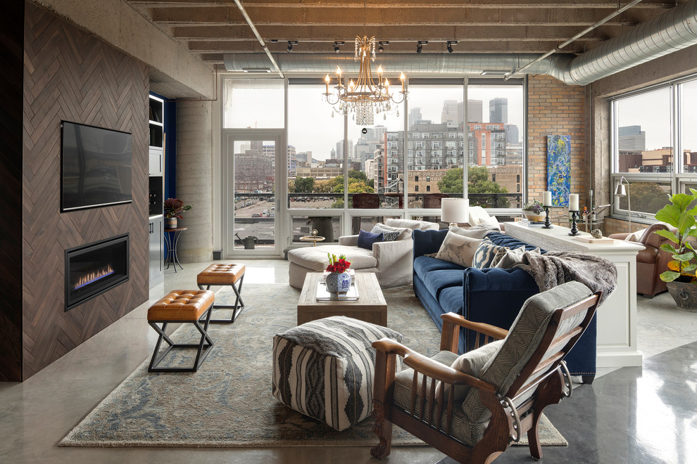 Источник вдохновения для домашнего уюта: большая открытая гостиная комната в стиле лофт с бетонным полом, серым полом, коричневыми стенами, горизонтальным камином, фасадом камина из дерева, телевизором на стене и синим диваном
