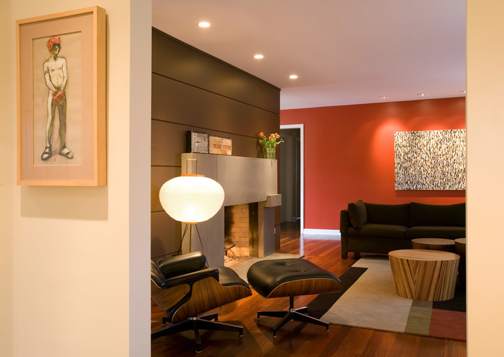Cette photo montre un salon moderne ouvert avec un mur rouge, un sol en bois brun, une cheminée standard et un manteau de cheminée en béton.