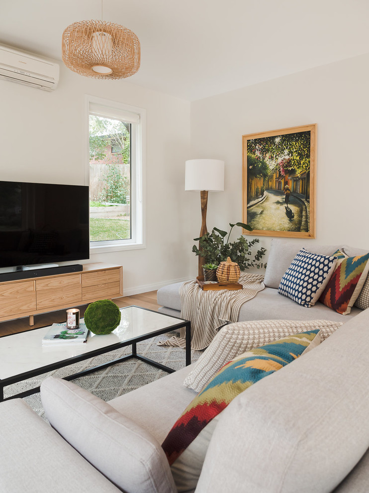 Modelo de salón abierto contemporáneo grande con paredes blancas, suelo de madera clara, televisor independiente y suelo marrón