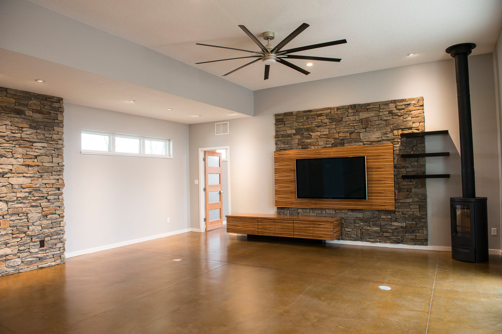 カンザスシティにある中くらいなミッドセンチュリースタイルのおしゃれなLDK (グレーの壁、コンクリートの床、薪ストーブ、コンクリートの暖炉まわり、壁掛け型テレビ、茶色い床) の写真