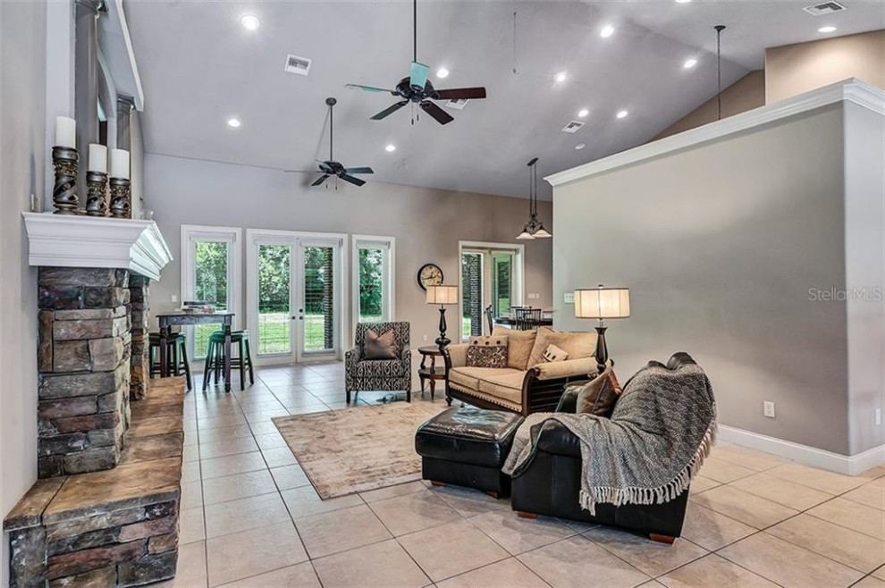 Inspiration for a large timeless open concept porcelain tile, beige floor and vaulted ceiling living room remodel in Orlando with beige walls, a ribbon fireplace and a stacked stone fireplace