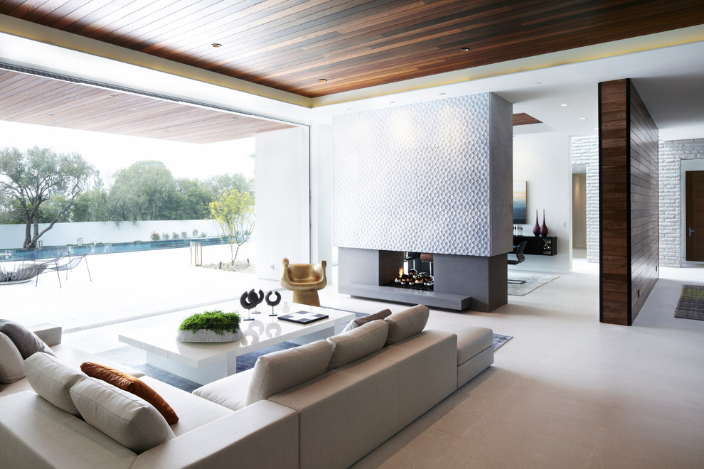 Cette photo montre un grand salon moderne ouvert avec un mur gris, un sol en carrelage de céramique, une cheminée double-face et un manteau de cheminée en pierre.