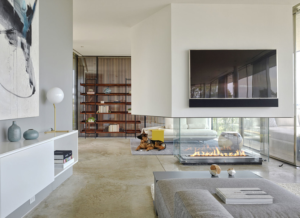 Idee per un soggiorno contemporaneo aperto con pareti bianche, pavimento in cemento, camino bifacciale e TV a parete